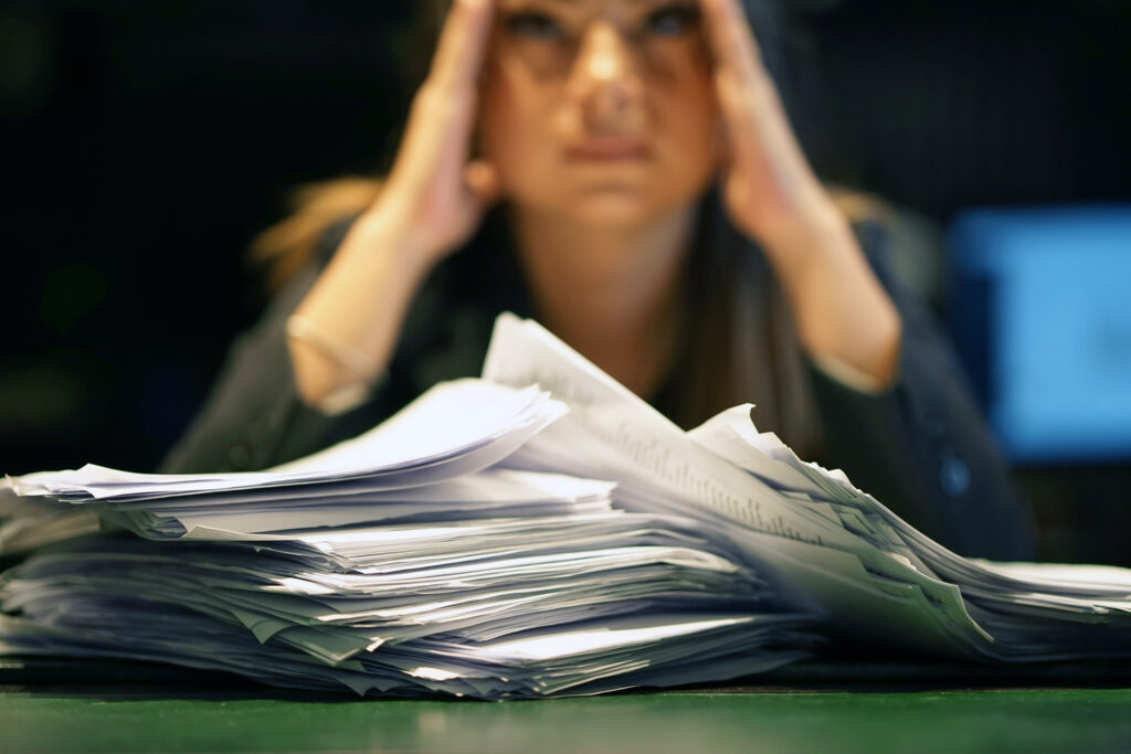 Close-up of a person who is distressed with a lot of paperwork in front of her.