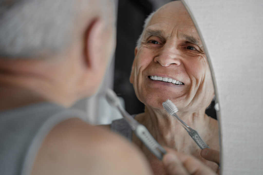 Smiling old man brushing his teeth with toothbrush.