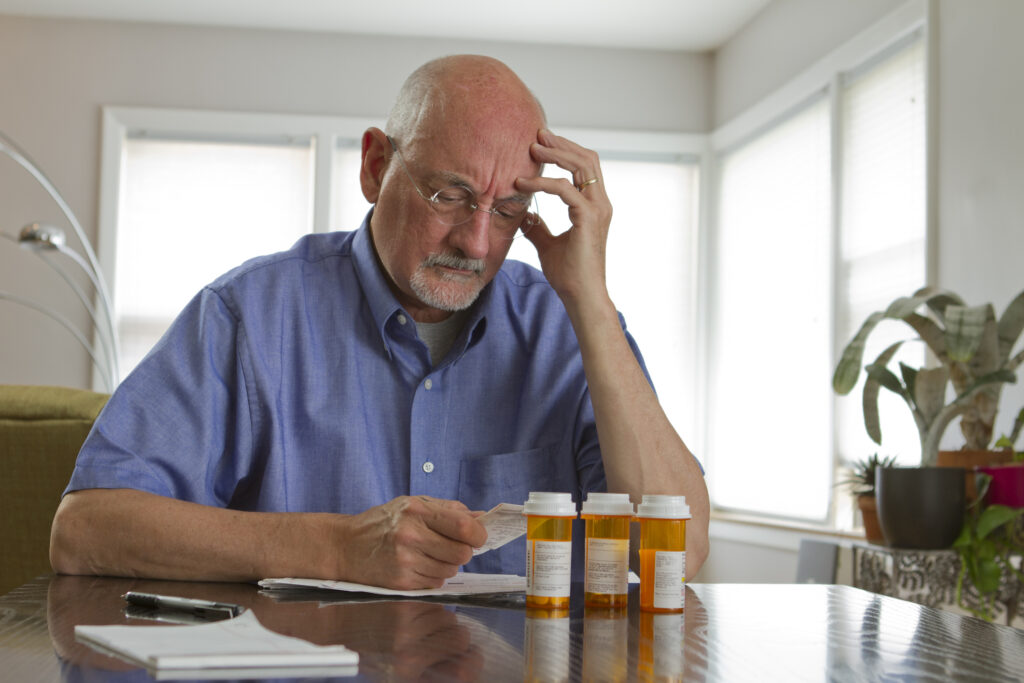 An older man with prescription bottles looking at a bill worried